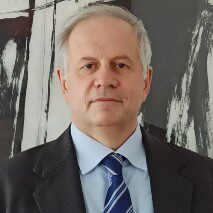 Portr&auml;tfoto eines &auml;lteren Mannes im Anzug mit blauer Krawatte vor abstraktem schwarz-wei&szlig;em Hintergrund.